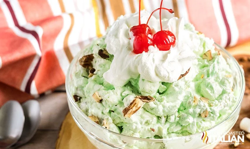 bowl of pistachio fluff topped with whipped cream and cherries