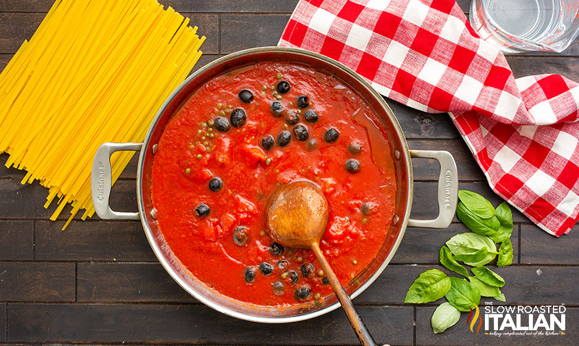 stirring olives and capers into tomato sauce