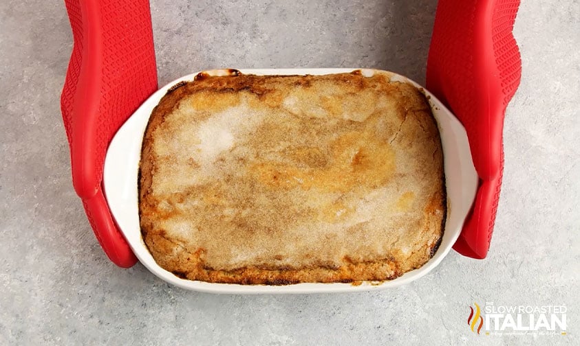 holding baked peach cobbler with red oven mitts