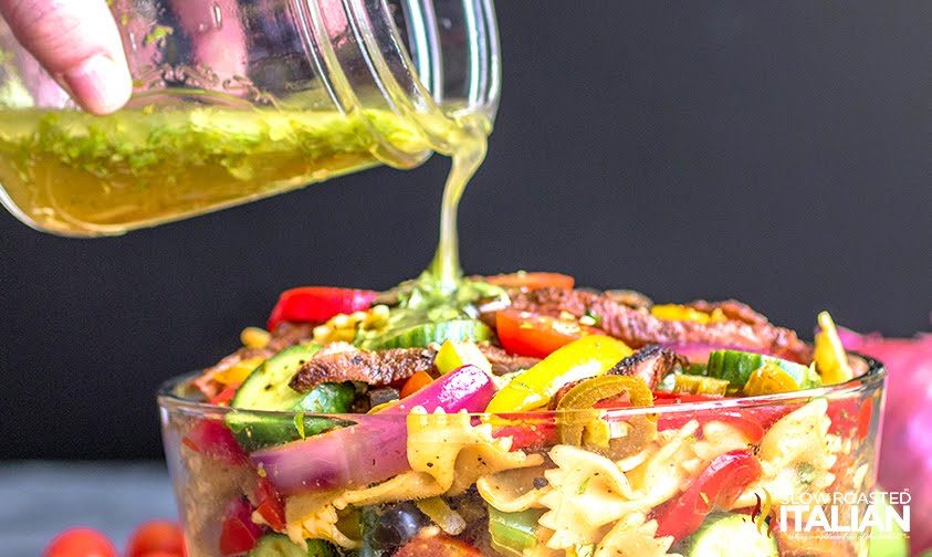 pouring dressing over pasta salad with steak