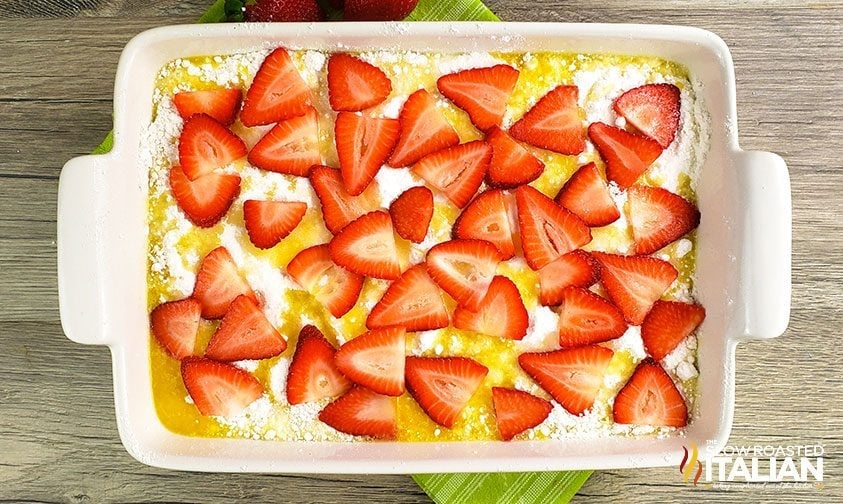 casserole dish with sliced strawberries over cake mix and melted butter