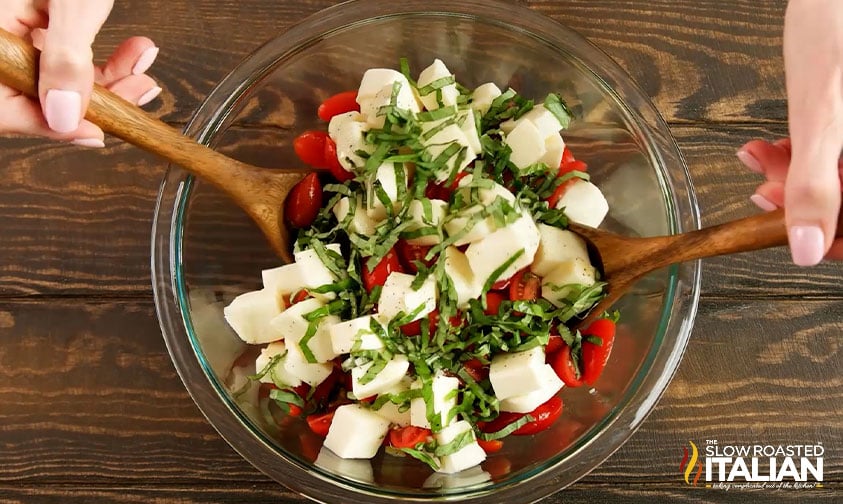 tossing tomatoes, mozzarella, and basil with wooden spoons