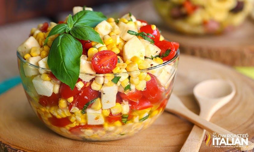 clear bowl of summer corn salad topped with fresh basil leaves
