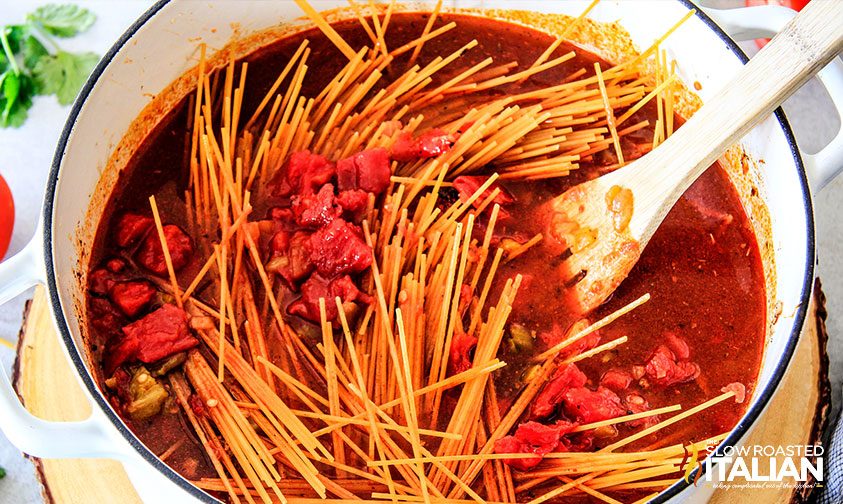 stirring dry spaghetti noodles into seasoned broth