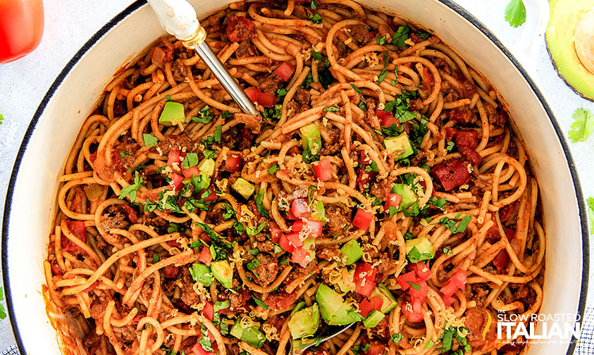 pot of taco spaghetti topped with tomatoes, cheese, and avocado