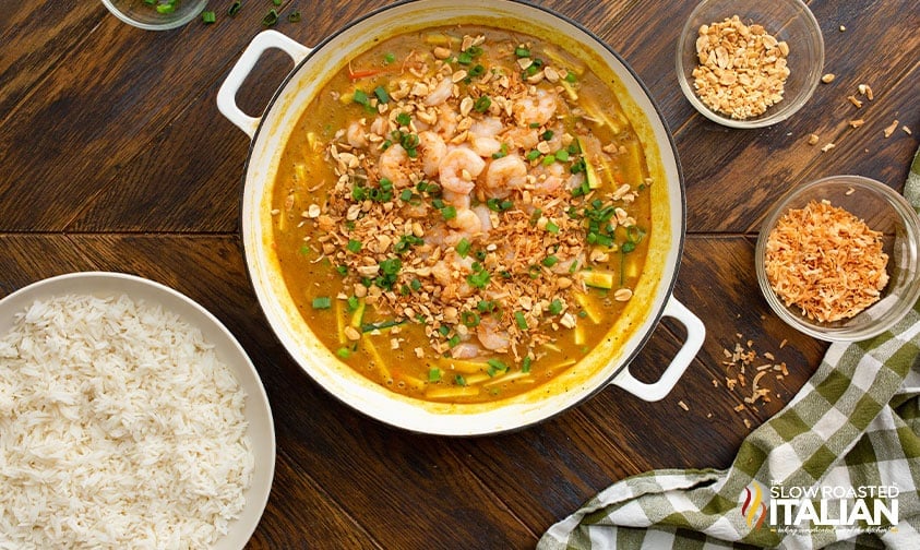 large pot of thai shrimp curry between bowls of cooked rice and toppings