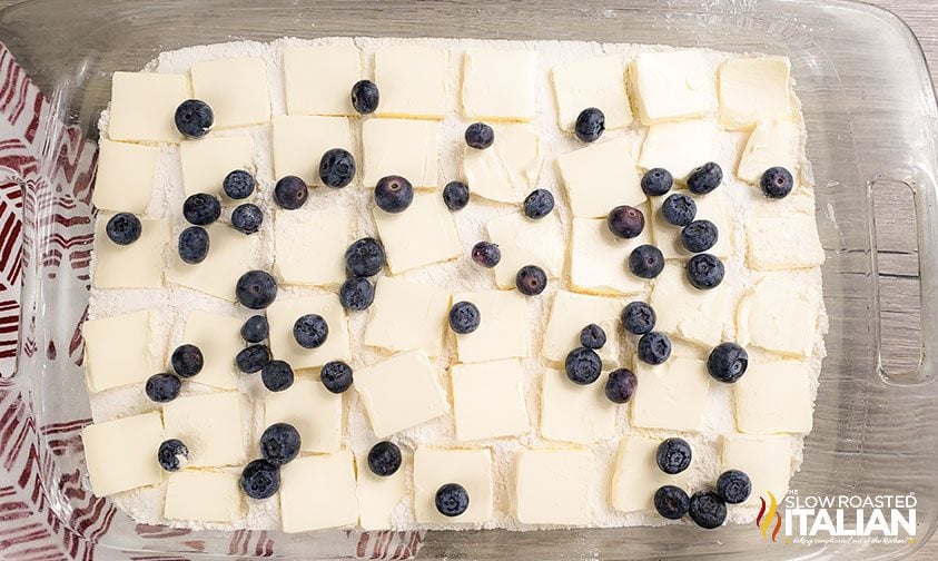 butter squares and blueberries scattered over cake mix and pie filling