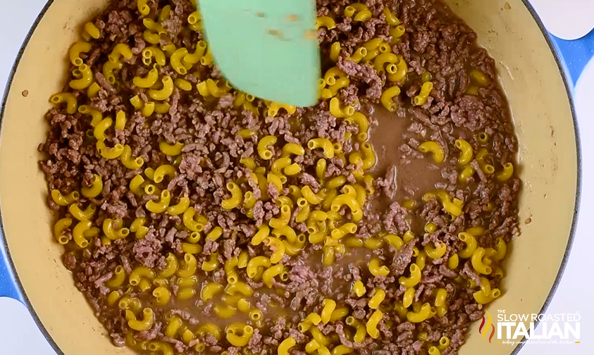 overhead: stirring uncooked macaroni with browned beef in a skillet