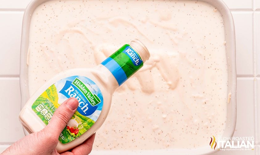 pouring bottle of ranch dressing over casserole in baking dish