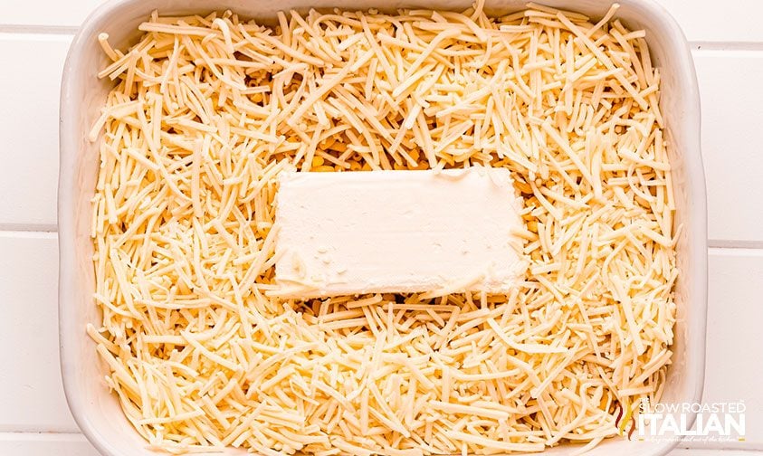 cream cheese in the center of a baking dish surrounded by shredded cheddar