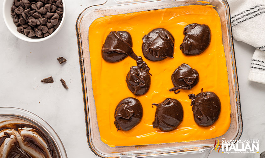 drops of brownie batter dotted over orange cheesecake layer