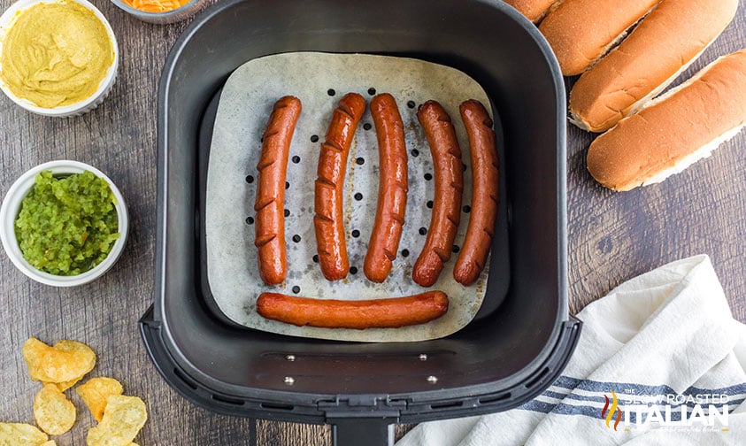 scored hot dogs in air fryer basket with parchment liner