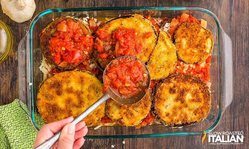 spooning tomato sauce over fried eggplant in baking dish