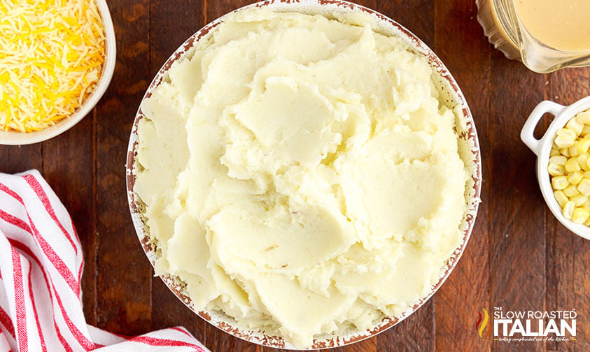 large bowl of mashed potatoes surrounded by cheese, corn, and gravy