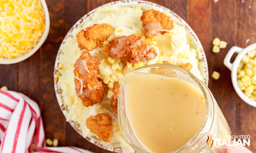 pouring gravy over bowl of mashed potatoes with chicken and corn
