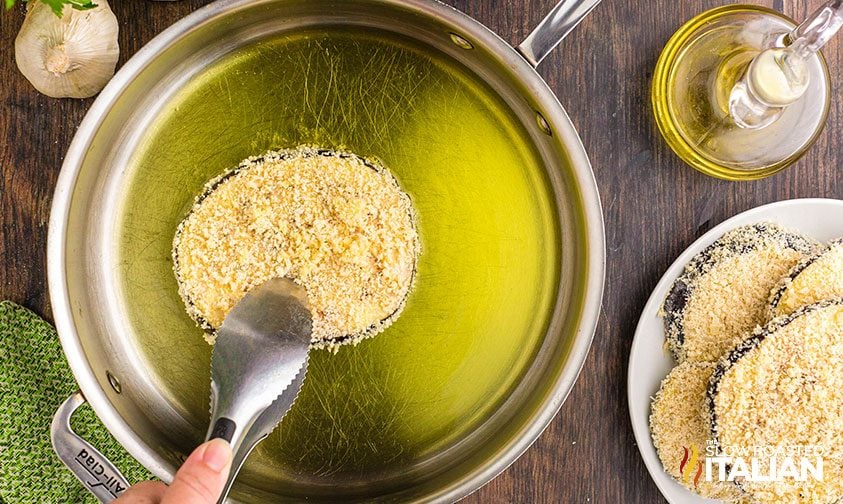 placing breaded eggplant slice in skillet with oil