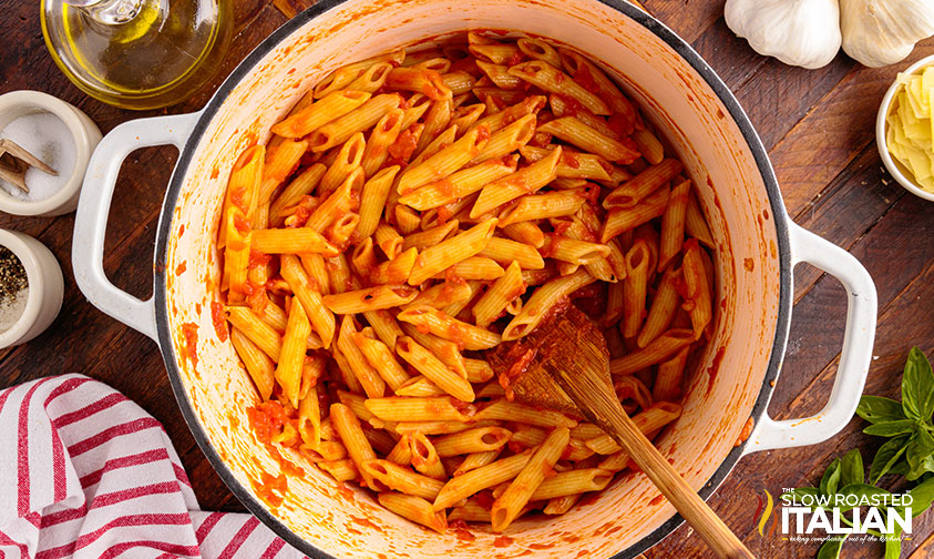 stirring penne noodles into tomato sauce