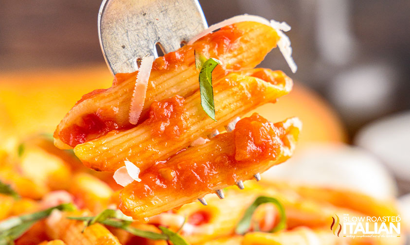 closeup: forkful of penne with tomato sauce, basil, and parmesan