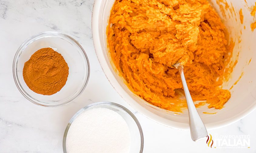 spoon in a bowl of pumpkin cookie dough next to bowls of cinnamon and sugar