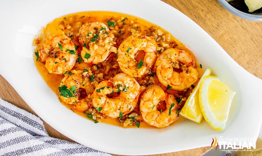 shrimp scampi in oval bowl with lemon wedges