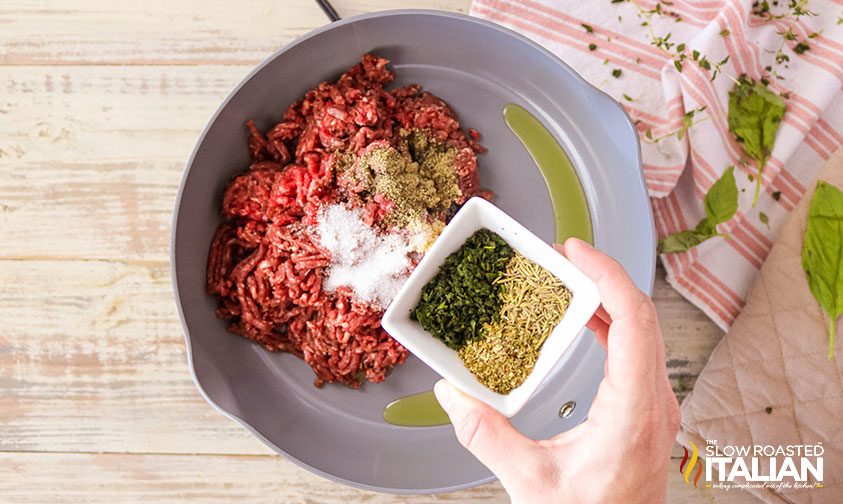 sprinkling herbs and spices over ground beef in skillet