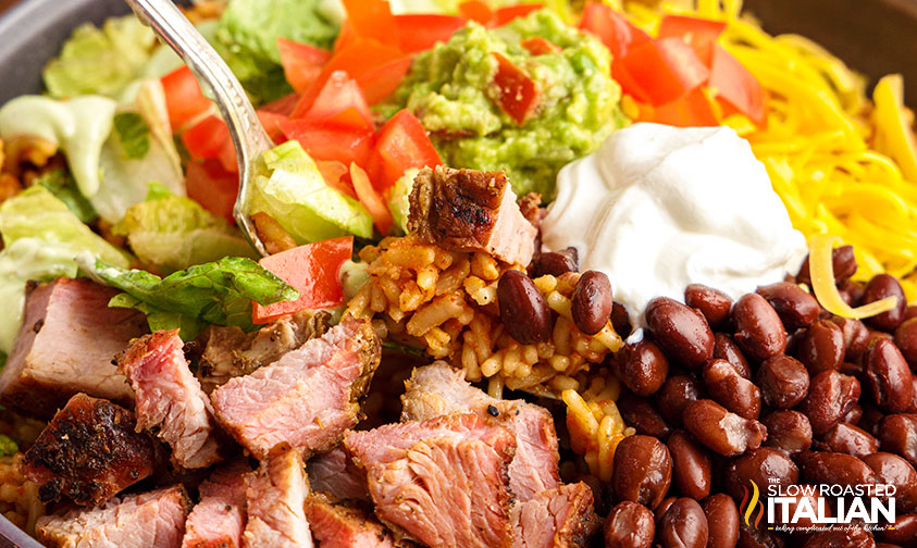 closeup: bowl of steak, beans, rice, cheese, and veggies with sour cream and guac