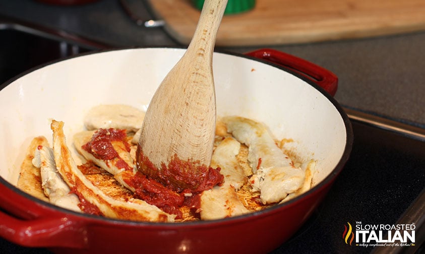 adding tomato paste to cooked chicken