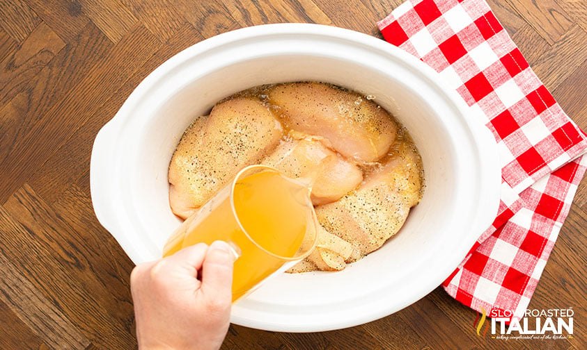 pouring chicken broth in crockpot with chicken breasts
