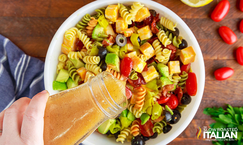 pouring italian dressing over pasta salad