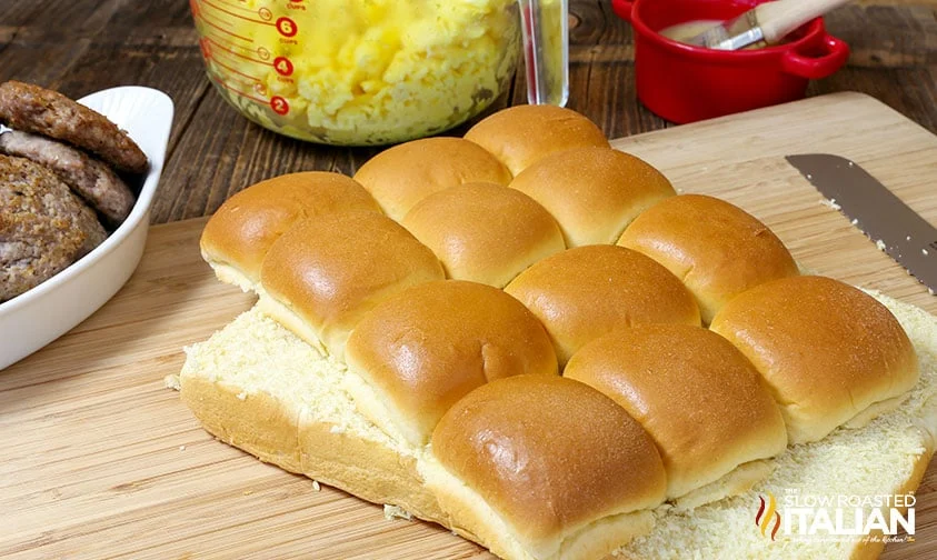 hawaiian rolls sliced for sliders with sausage and eggs in background