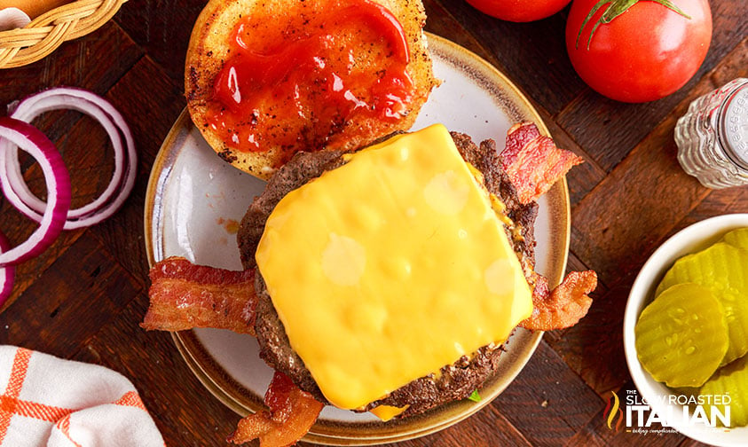 burger patty with cheese on bacon strips with top bun smeared in ketchup