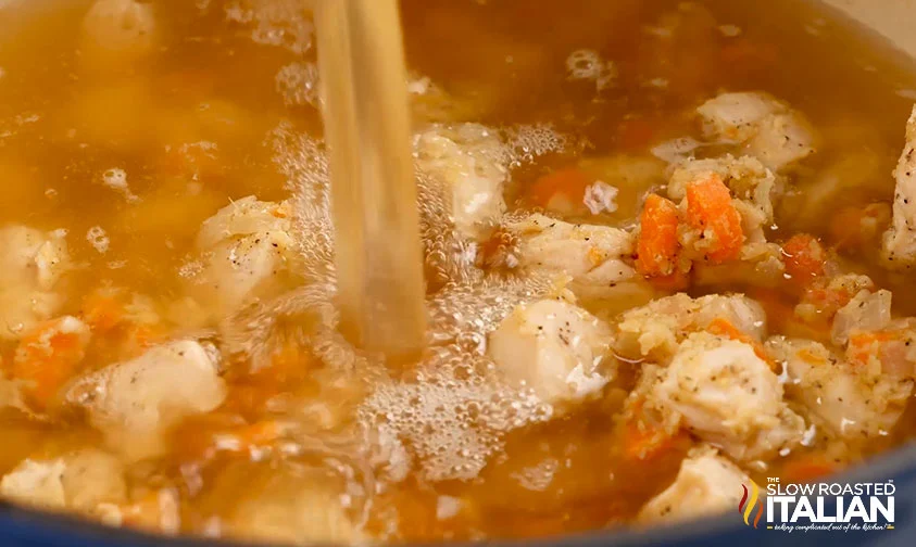 pouring broth into pot with chicken and veggies