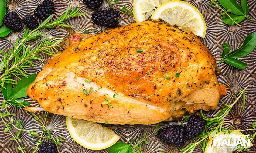 cooked turkey breast surrounded by lemons, blackberries, and herbs