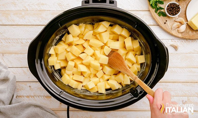 stirring chopped potatoes in crockpot