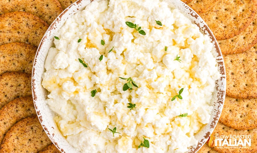 closeup: ricotta in bowl with thyme leaves surrounded by crackers