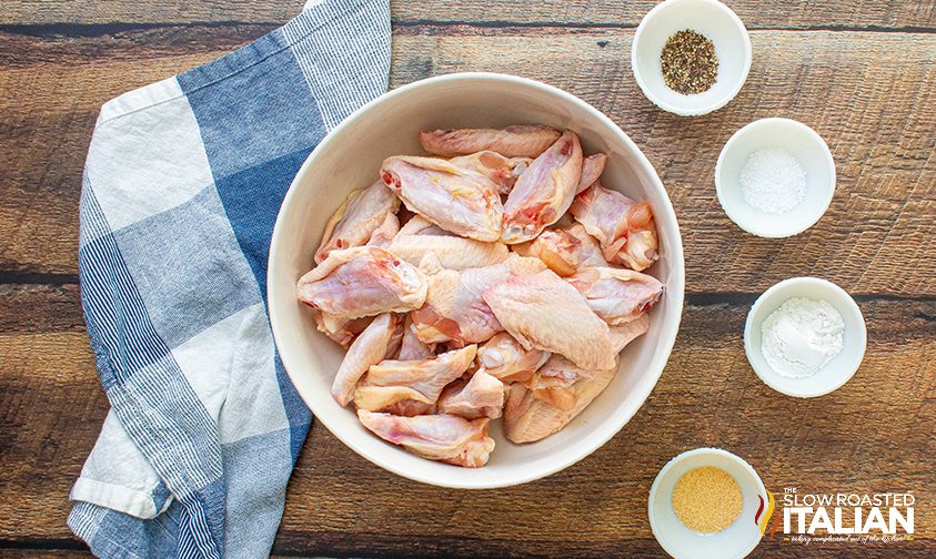 bowl of uncooked chicken wings with smaller bowls of spices