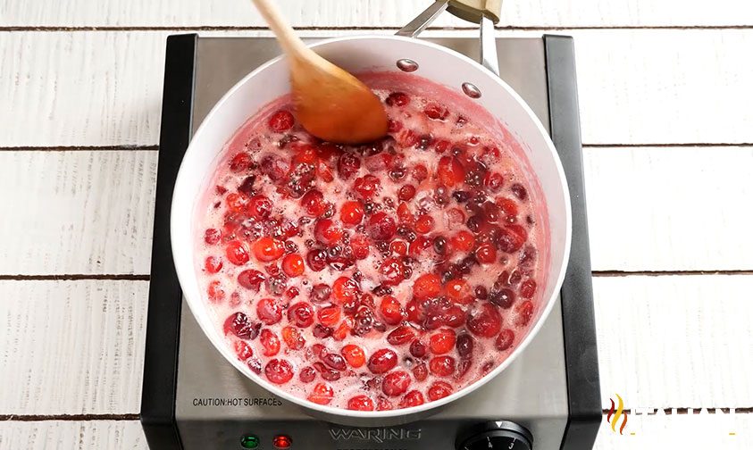 stirring cranberries as they simmer in saucepan