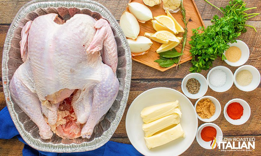 whole turkey in roasting pan next to onion, lemon, herbs, and spices, and butter