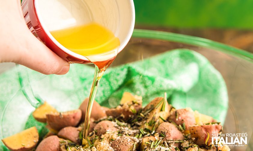 pouring oil over seasoned red potatoes in bowl