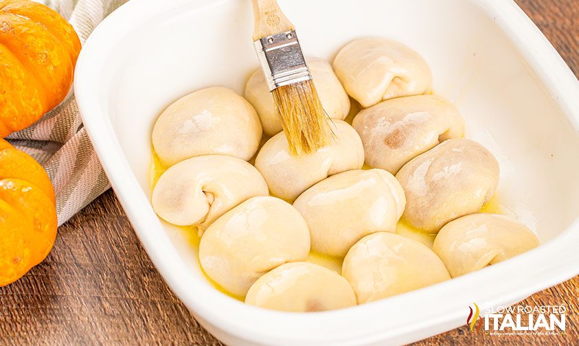 brushing glaze over pumpkin stuffed rolls in baking pan