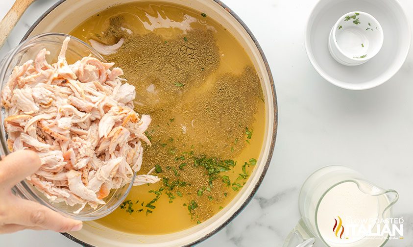 adding shredded turkey to pot with soup ingredients
