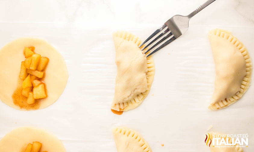 filling dough with apple filling and closing hand pies with fork