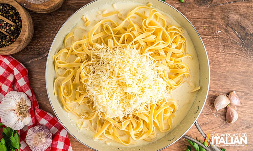 adding shredded cheese to fettucine in a skillet with sauce