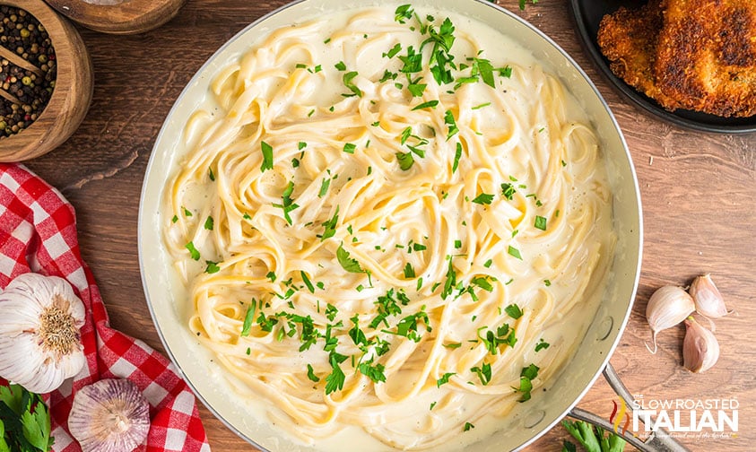 adding herbs to pasta with sauce in skillet