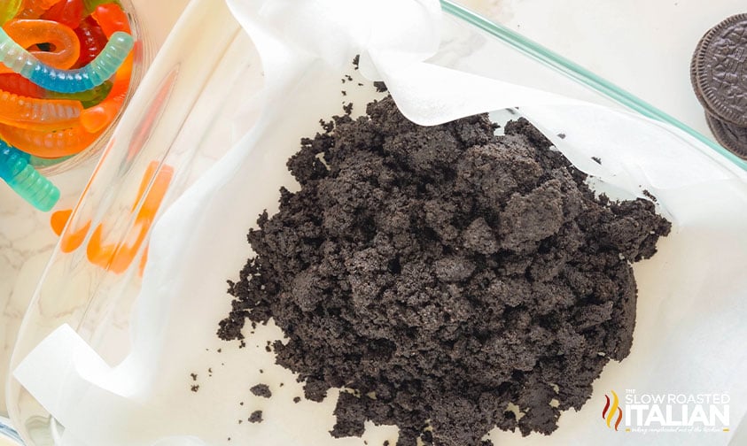 adding crushed oreos to baking pan for crust