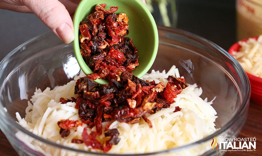 adding sun dried tomatoes to hashbrowns in a glass bowl