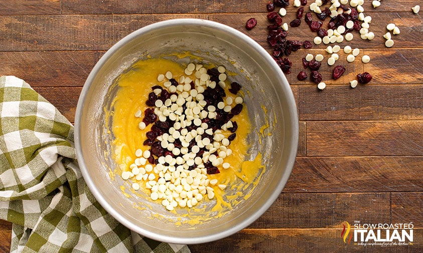 adding cranberries and white chocolate chips to mixing bowl