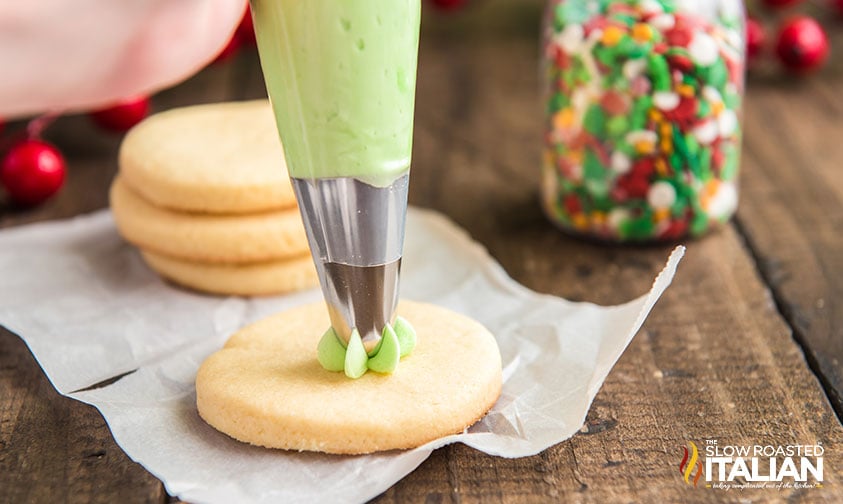 piping green frosting onto round cookie with star tip