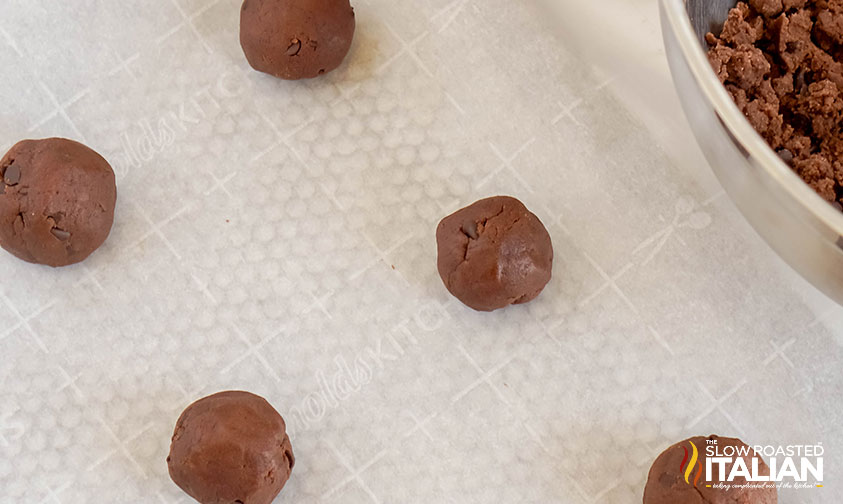 chocolate thumbprint cookie dough on parchment lined baking sheet