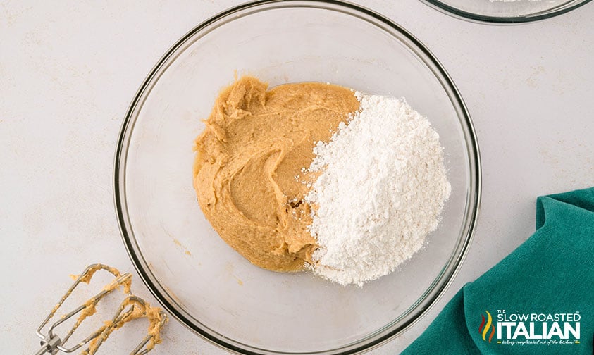 adding flour to creamed butter and sugars in a mixing bowl